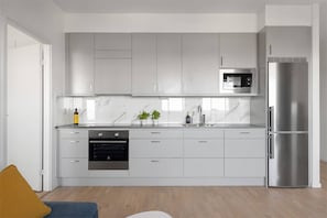 A modern kitchen with white cabinets, a stainless steel refrigerator, an oven, and a microwave.