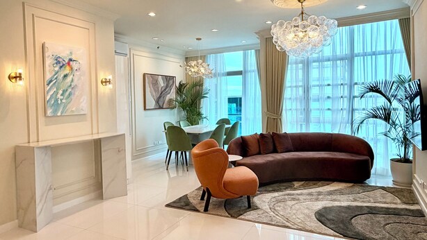 Una sala de estar moderna con un sofá curvo, un sillón naranja pequeño, una araña y obras de arte en las paredes.