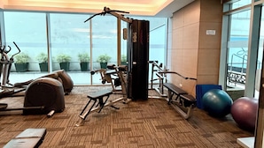 Un gimnasio con equipo de ejercicio, una banca y ventanas amplias que ofrecen vistas.