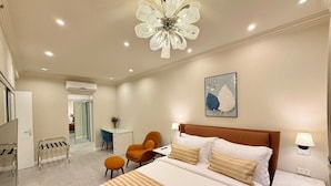 Una habitación de hotel moderna con una cama grande, un escritorio, una silla naranja y una lámpara decorativa en el techo.