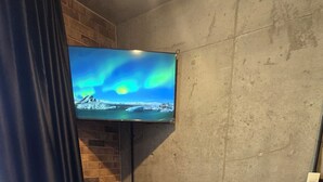 Ein modernes Zimmer mit einem großen Bett, einem an einer Ziegelwand befestigten Fernseher und einem Fenster mit Vorhängen.