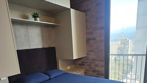 Ein modernes Schlafzimmer mit einem großen Bett, integrierten Stauraum, einer kleinen Pflanze und Blick auf die Stadt.