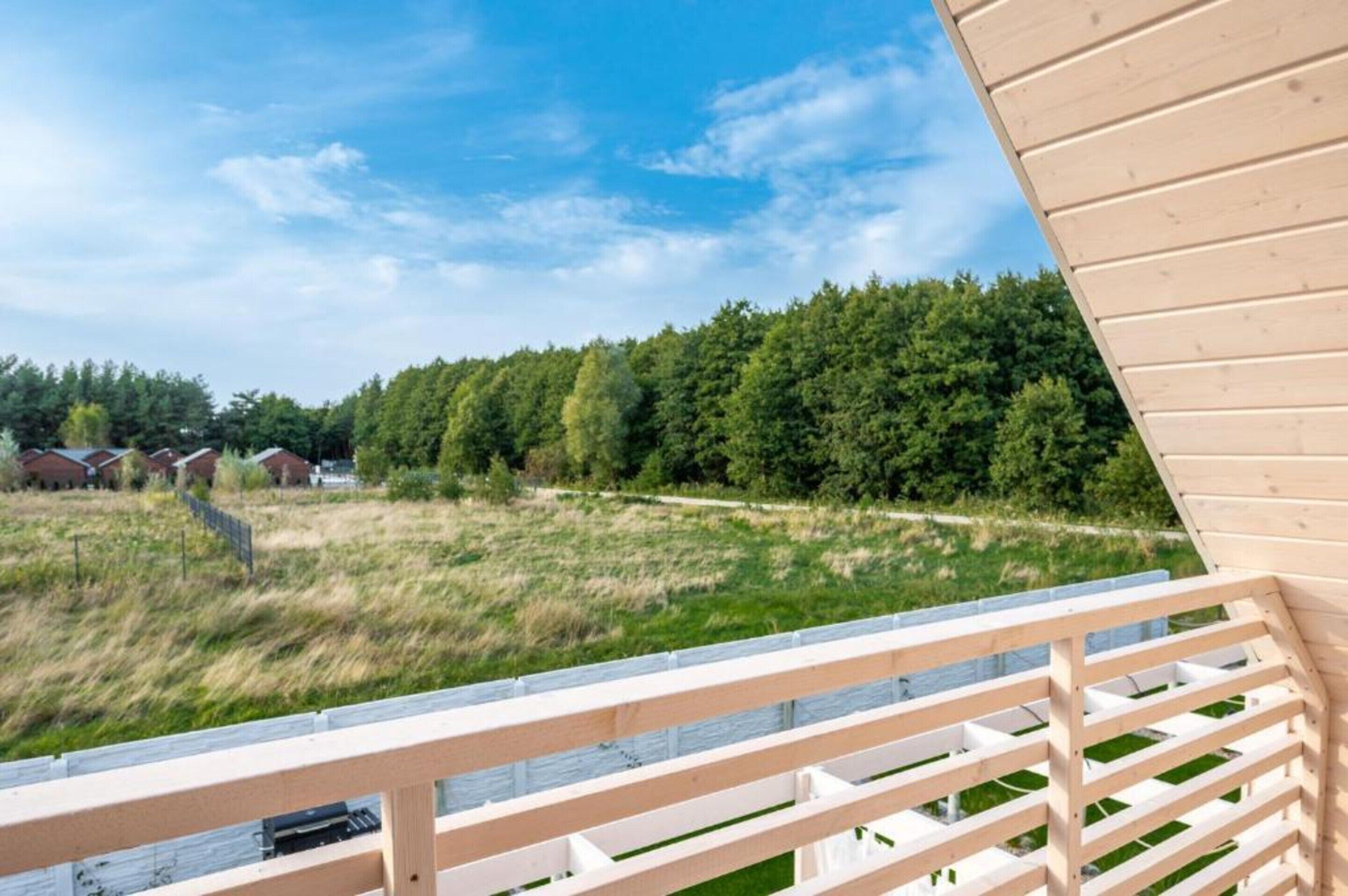 A wooden deck with a view of a grassy field and a row of houses in the background.