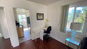 Habitación con escritorio, silla, lámpara y ventana con cortinas. Se ve una puerta que da a otra habitación.