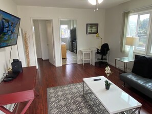 A living room with a red table, a white sofa, a patterned rug, and a TV on the wall. - Charming 2-bedroom apartment near Venice, SMC (Santa Monica)