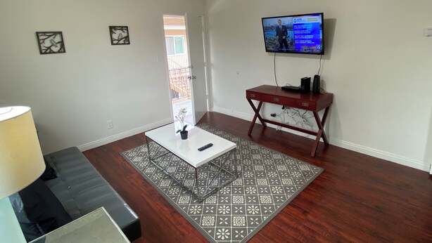 Una sala de estar con televisor, mesa de centro, sofá, alfombra estampada y ventilador de techo.