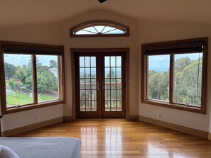 Ein geräumiges Zimmer mit großen Fenstern, Holzboden und Blick auf eine grüne Landschaft.