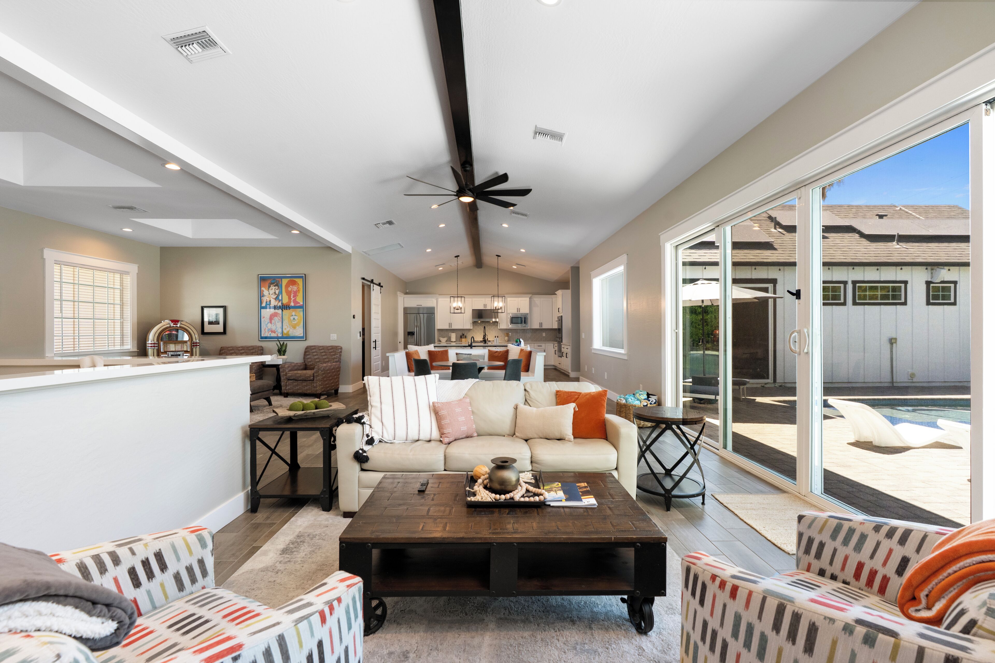 A spacious living area with a large sliding glass door leading to a backyard, a ceiling fan, and a kitchen in the background.
