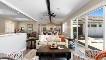 A spacious living area with a large sliding glass door leading to a backyard, a ceiling fan, and a kitchen in the background.