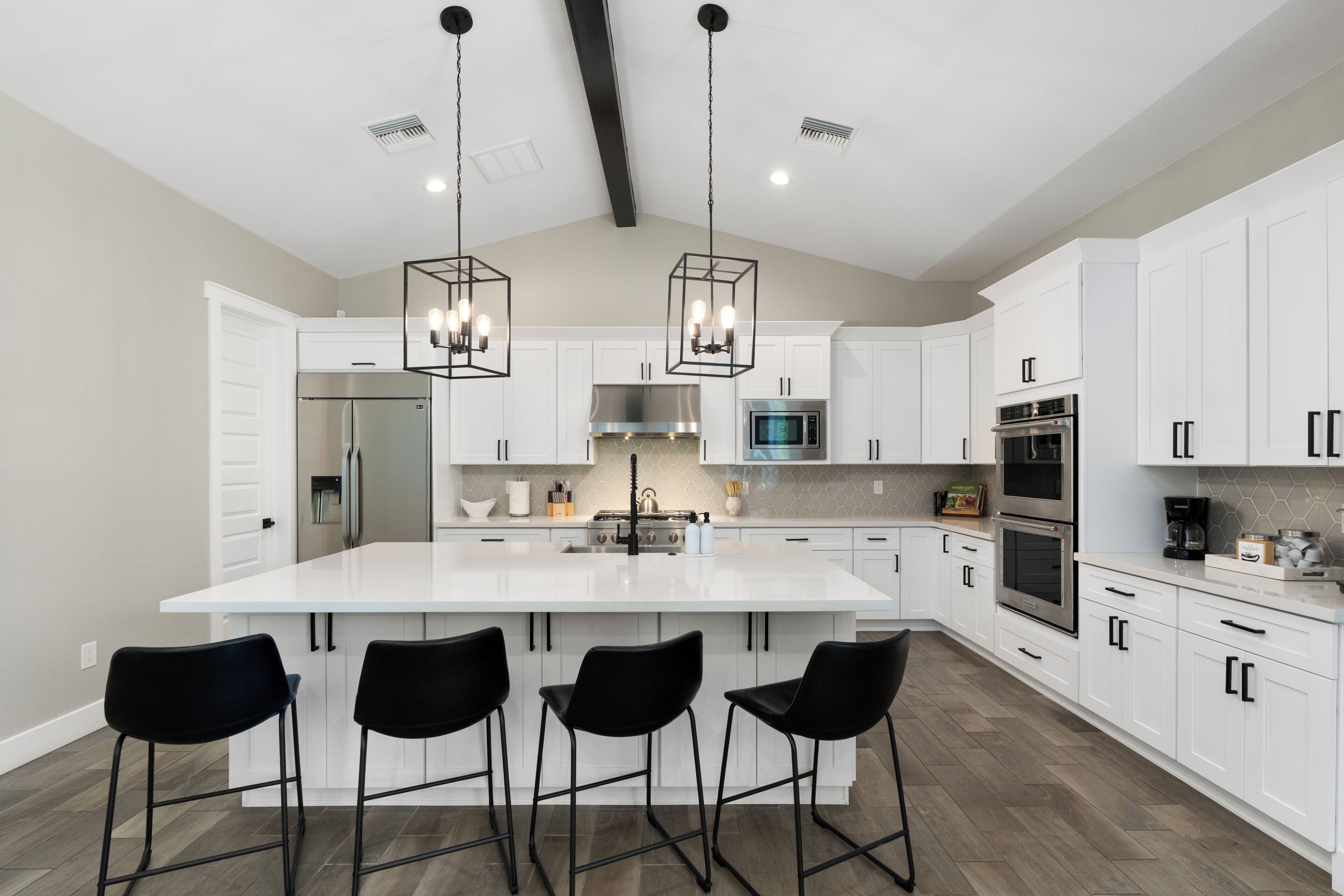 A modern kitchen with white cabinets, a large island with bar stools, stainless steel appliances, and pendant lighting.