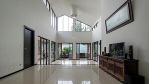Una habitación amplia con techo alto, ventanas grandes, un armario de madera con altavoces y un cuadro en la pared.