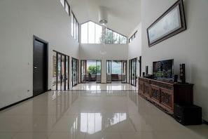 A spacious room with a high ceiling, large windows, a wooden cabinet with speakers, and a framed picture on the wall.