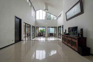 Um quarto espaçoso com teto alto, janelas amplas, um armário de madeira com alto-falantes e um quadro pendurado na parede.