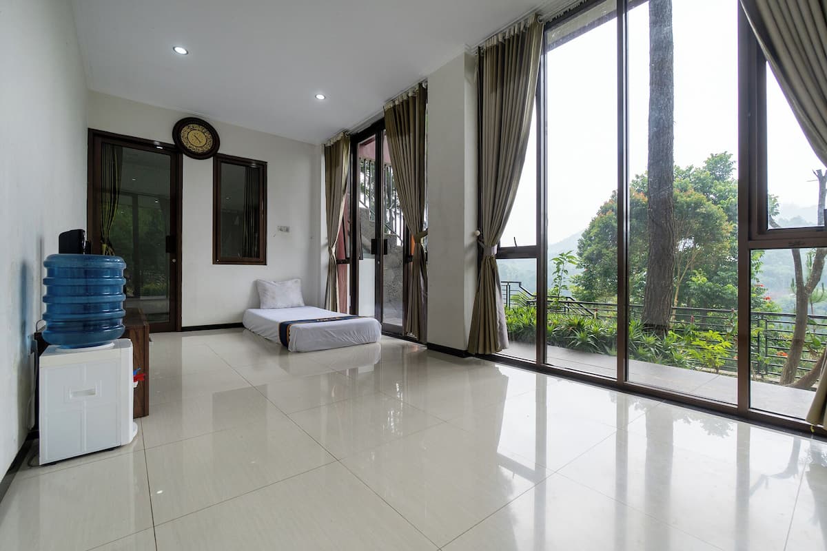 A spacious room with a bed, a water dispenser, a clock, and large windows offering a view of greenery.