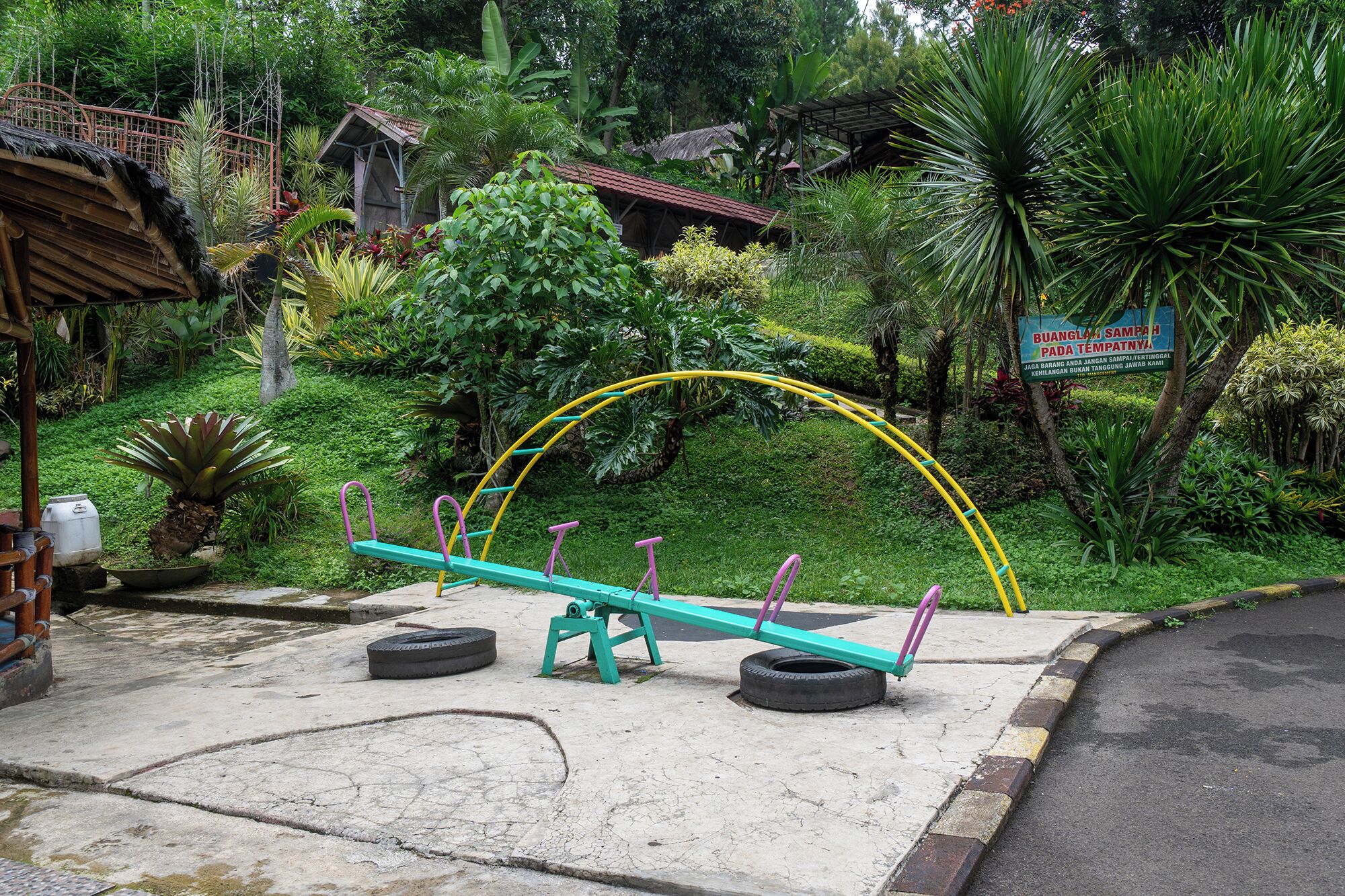 A seesaw in a garden with a sign in the background.