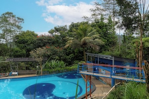 Una piscina con cubierta azul y una pequeña estructura azul, rodeada de abundante vegetación y árboles.
