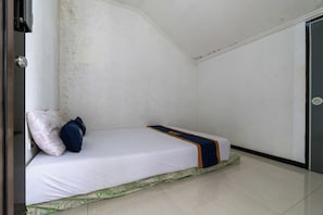 A small, single-bed room with a white mattress, a blue and orange blanket, and a green patterned bed skirt.