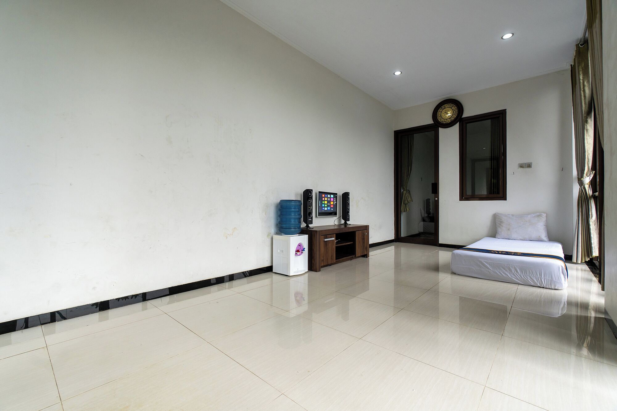 A hotel room with a bed, a TV, a water dispenser, and a clock on the wall.