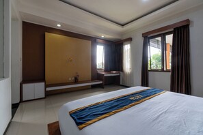 A hotel room with a bed, a desk, a window with curtains, a built-in wardrobe, and a small potted plant.