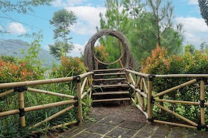 A bamboo bridge with a circular arch structure, surrounded by greenery and trees.