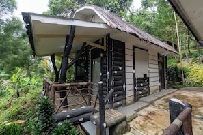 A rustic wooden structure with a thatched roof, surrounded by lush greenery.