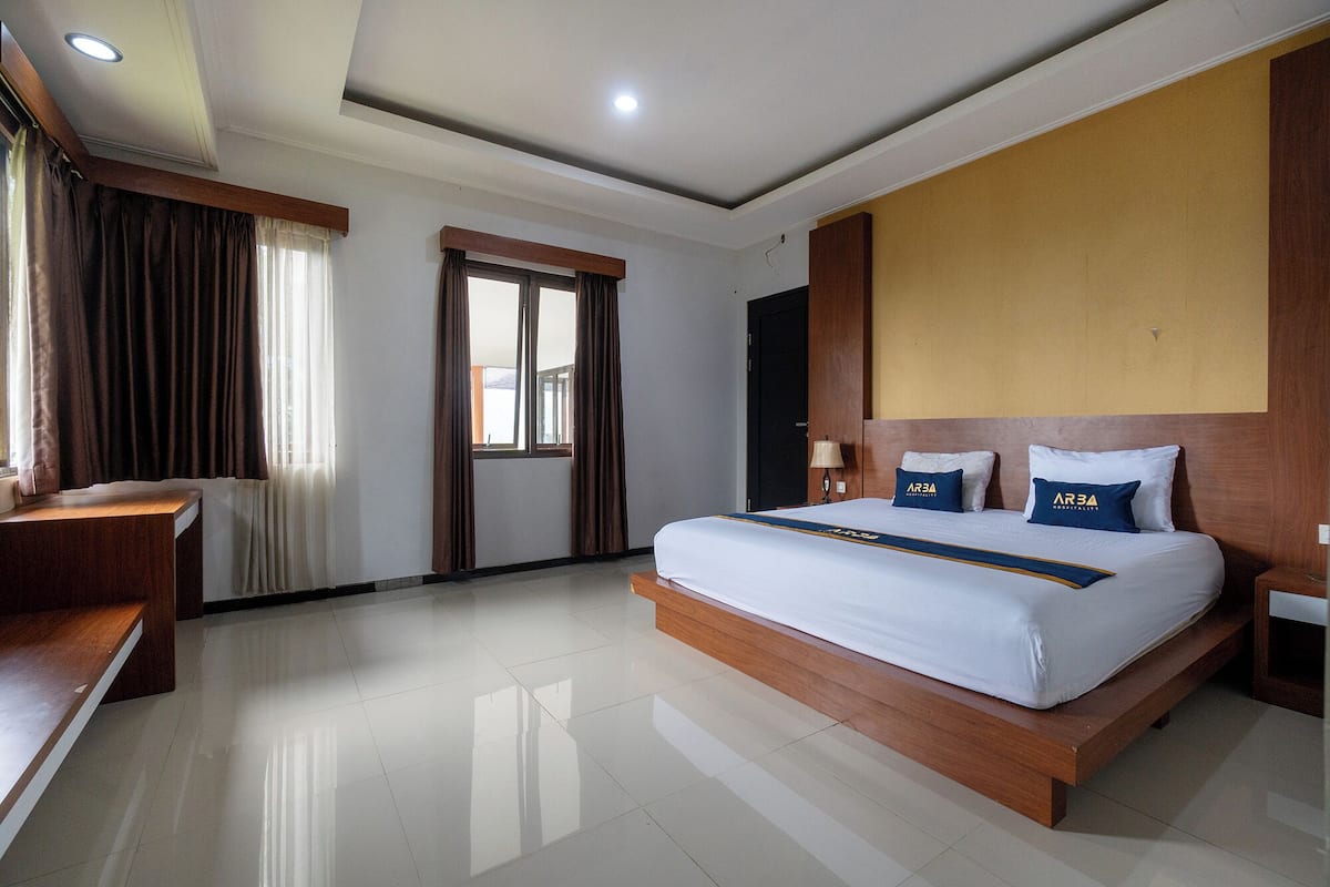 A hotel room with a large bed, a desk, a window with curtains, and a door.