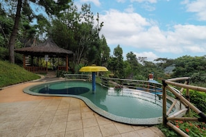 Una piscina con borde curvo, un pabellón de techo de paja y una valla de bambú.