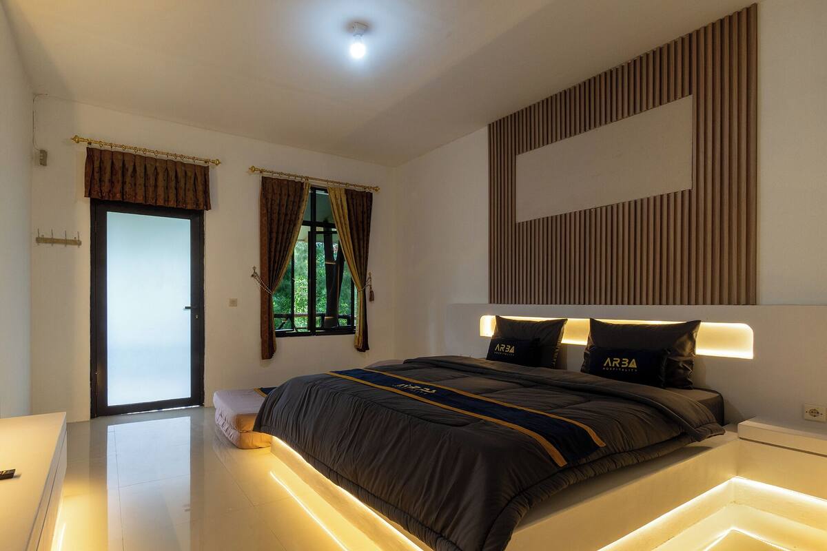 A modern bedroom with a bed, bedside lamps, and a view of the outdoors.