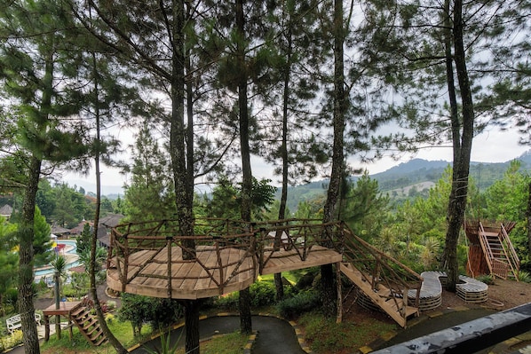 A wooden observation deck surrounded by trees, with a pool and lounge chairs in the background.