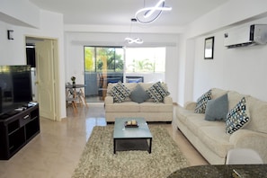 Sala de estar com sofá, mesa de centro, televisão e varanda com mobiliário de exterior.