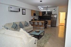 Una sala de estar moderna con un sofá, una mesa de centro y una zona de cocina con refrigerador, microondas y estufa.