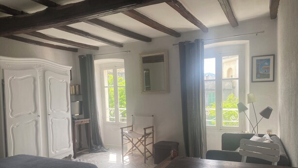A room with a bed, a table, a chair, a wardrobe, and a window with a view of greenery.