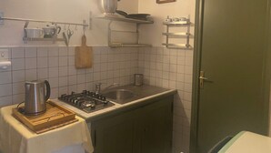 A kitchen with a gas stove, a kettle, a sink, and a wooden cutting board.