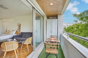 A balcony with a dining table, chairs, and a sofa in the adjacent room. - Charming Studio Bercy Village/accor Arena (Paris)