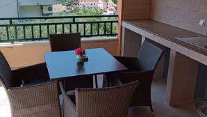 Ein Balkon mit Tisch und Stühlen, Blick auf Gebäude und das Meer, sowie eine Küchenzeile.
