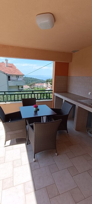 Ein Balkon mit Tisch und Stühlen, Blick auf Gebäude und das Meer, sowie eine Küchenzeile.