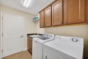 A laundry room with a washer and dryer, wooden cabinets, a white door, and a countertop with a sink. - 3-bedroom house in The Villages with Golf Cart between Sumter and Brownwood (The Villages)