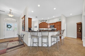 A modern kitchen with a central island, bar stools, wooden cabinets, and a microwave. - 3-bedroom house in The Villages with Golf Cart between Sumter and Brownwood (The Villages)