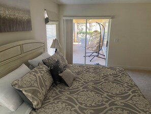 A bedroom with a large bed, a headboard, a bedside lamp, and a view of an outdoor seating area through a sliding glass door. - 3-bedroom house in The Villages with Golf Cart between Sumter and Brownwood (The Villages)