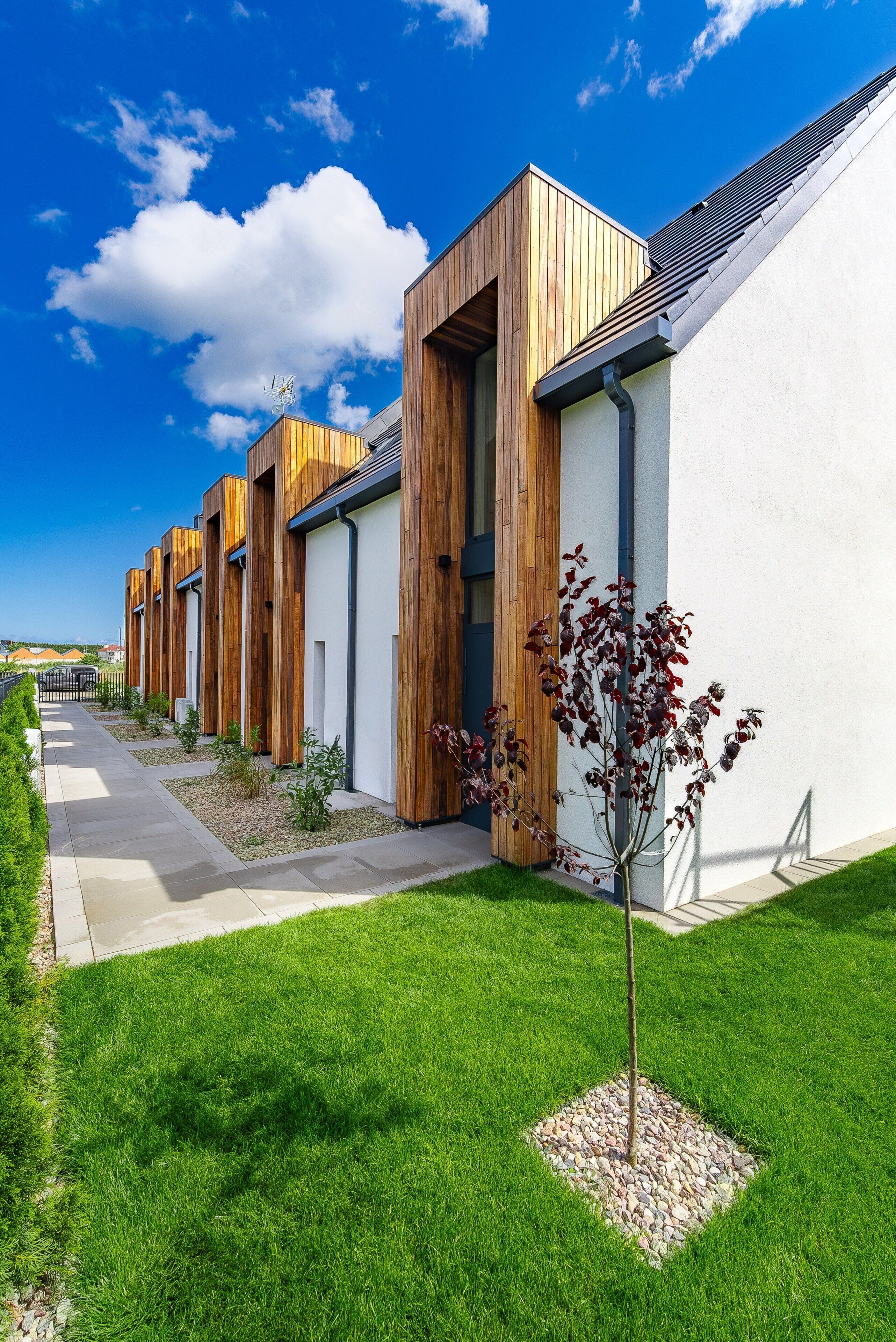 A row of modern buildings with wooden facades and white walls, a clear sky, and a well-maintained lawn.