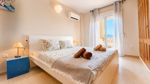 A bedroom with a bed, bedside tables, an air conditioning unit, a window with curtains, and a view of the outside. - Casa Ideal | Valle del Este, Vera (Vera)