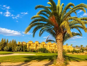A palm tree, a golf course, and a yellow building with multiple windows. - Casa Ideal | Valle del Este, Vera (Vera)