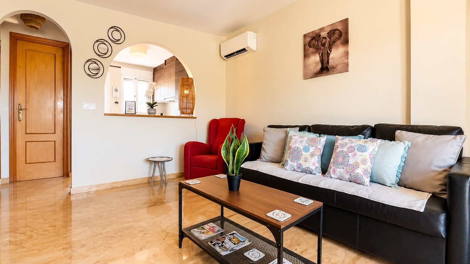 A living room with a sofa, red chair, coffee table, and a wall-mounted picture.