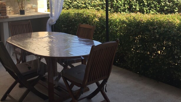 Une terrasse extérieure avec une table ronde et des chaises, un luminaire suspendu et une vue sur une colline parsemée de bâtiments.