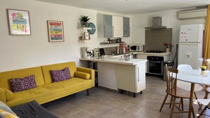 Une cuisine moderne avec des meubles blancs, un canapé jaune et un coin repas comprenant une table et des chaises.