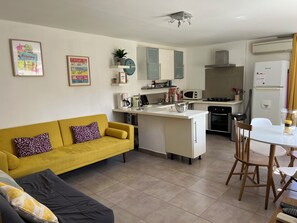 A modern kitchen with white cabinets, a yellow sofa, and a dining area with a table and chairs. - Charming rental Casabianca Sartene South Corsica, T2 apartment in a quiet area (Sartène)