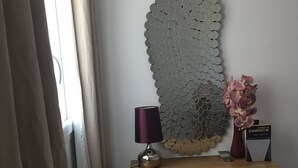Une pièce comprenant une console en bois, un élément décoratif mural, une lampe violette, un vase avec des fleurs roses et un livre intitulé « Une chambre avec vue ».
