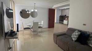 Ein modernes Wohnzimmer mit Sofa, Essbereich mit Glastisch und Küchenzeile.