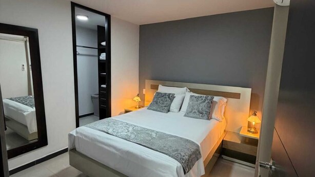 Ein modernes Schlafzimmer mit einem großen Bett, Nachttischlampen, einem Spiegel und einem Kleiderschrank.