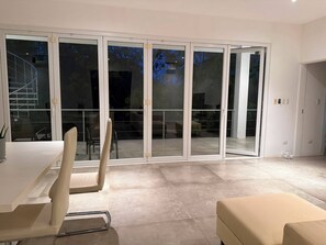 En modern inredning med ett matområde, en soffa och en skjutdörr i glas som leder ut till ett utomhusområde.